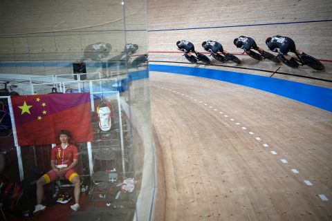 Cyclists from New Zealand competes in a team pursuit heat while China's Zhong Tianshi, left, takes a break on August 2.