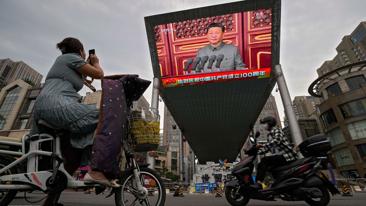 A woman on her electric-powered scooter films a large video screen outside a shopping mall showing Chinese President Xi Jinping speaking during an event to commemorate the 100th anniversary of China's Communist Party at Tiananmen Square in Beijing, Thursday, July 1, 2021.
