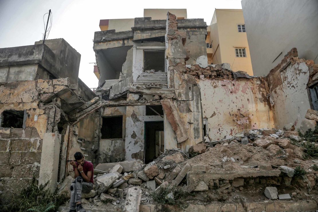 A man sits in the rubble of a destroyed house near the port, almost a year after the blast.