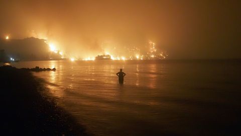 A man watches from the water as a wildfire approaches Kochyli beach near Limni village on Evia island.