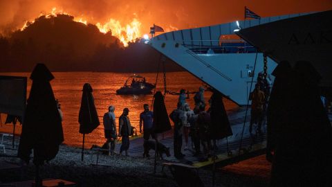 People are evacuated on a ferry as a wildfire burns in Limni.
