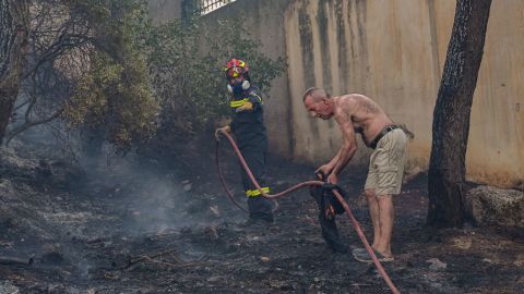 A resident helps a firefighter before fire spreads to houses in the Thrakomacedones area of Athens, Greece on August 7.