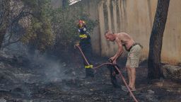 ATHENS, GREECE - AUGUST 7: A local resident helps a firefighter to battle fire before it spreads to houses in Thrakomacedones area, in northern Athens, on August 7, 2021 in Athens, Greece. People were evacuated from their homes after a wildfire reached residential areas of northern Athens as record temperatures were recorded at 42 degrees Celsius (107.6 Fahrenheit). (Photo by Milos Bicanski/Getty Images)