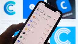 This illustration photo shows the Coinbase logo in the background as a person checks cryptocurrencies prizes on a smartphone in Los Angeles on April 13, 2021. - The arrival April 13, 2021, of cryptocurrency exchange Coinbase on Nasdaq is one of the most anticipated events of the year on Wall Street, where enthusiasm for record-breaking bitcoin is in full swing, despite questions about the sustainability of the market. (Photo by Chris DELMAS / AFP) (Photo by CHRIS DELMAS/AFP via Getty Images)