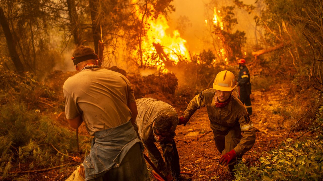 Firefighters and volunteers use a water hose near a burning blaze trying to extinguish a fire in the village of Glatsona on Evia island, on August 9.