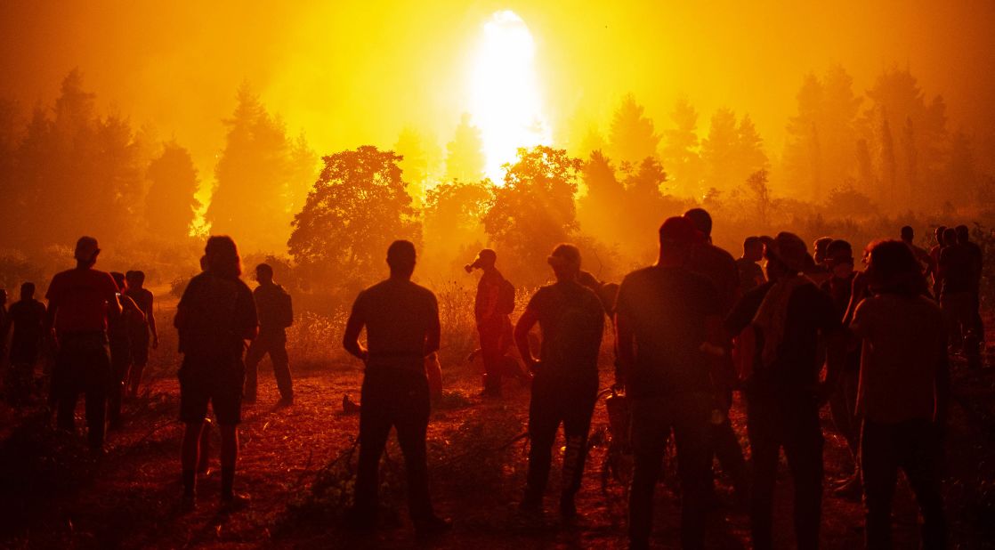 Local youths and volunteers gather in a field and wait to support firefighters during a wildfire on August 9, close to the village of Kamatriades on the Greek island of Evia.