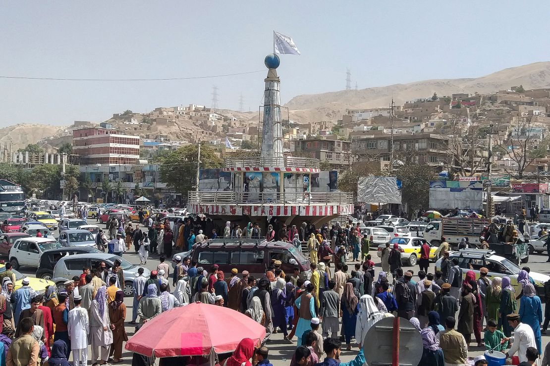 A Taliban flag is seen on a plinth with people gathered around the main city square at Pul-e-Khumri on August 11, 2021 after Taliban captured Pul-e-Khumri, the capital of Baghlan province.