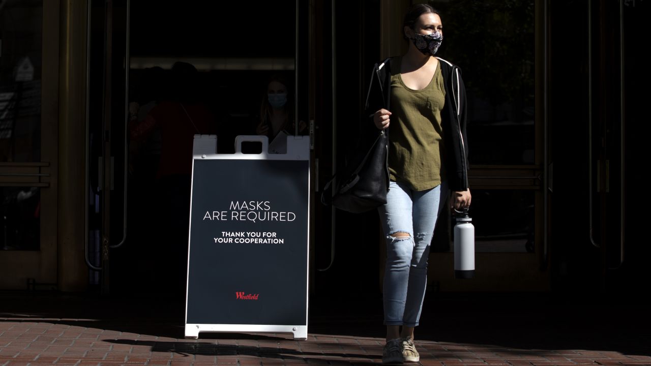 A woman walks by a sign reading 'Masks Are Required' outside a shopping mall on August 3, 2021, in San Francisco.