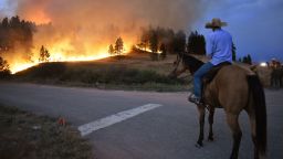 Rowdy Alexander watches from atop his horse as a hillside burns on the Northern Cheyenne Indian Reservation, Wednesday, Aug 11, 2021, near Lame Deer, Mont. The Richard Spring fire was threatening hundreds of homes as it burned across the reservation. (AP Photo/Matthew Brown)
