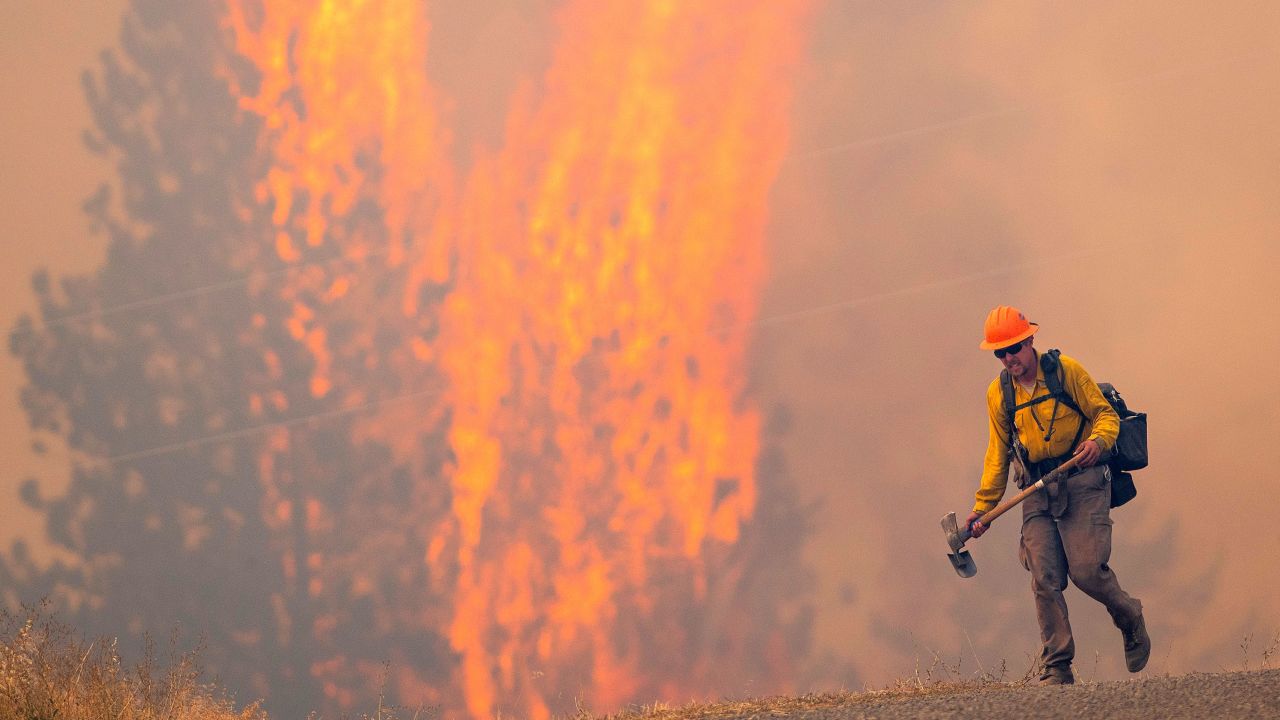 After walking down a gravel road to do recon on a fire cresting into the trees, a wildland firefighter grimaces as he walks back to his crew on August 12, 2021, at the Bedrock Fire north of Lenore, Idaho. 