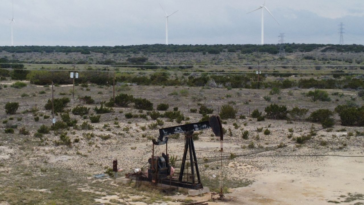Blades from wind turbines rotate in a field behind an out-of-use oil pumpjack, April 16, 2021 near Eldorado, Texas. 