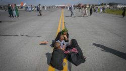 Afghan people sit along the tarmac as they wait to leave the Kabul airport in Kabul on August 16, 2021, after a stunningly swift end to Afghanistan's 20-year war, as thousands of people mobbed the city's airport trying to flee the group's feared hardline brand of Islamist rule. (Photo by Wakil Kohsar / AFP) (Photo by WAKIL KOHSAR/AFP via Getty Images)