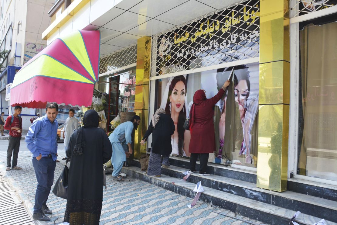 Workers at a beauty salon strip large photos of women off the wall in Kabul on August 15, 2021.