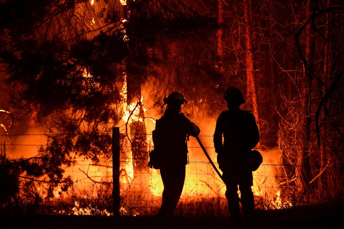Firefighters spray water on trees during the Dixie Fire, which was caused by damage to power lines, in August 2021 near Janesville, California.