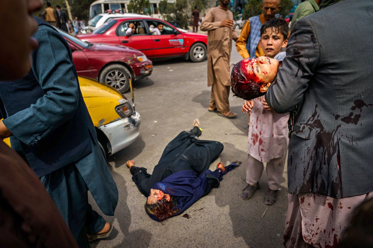 A man carries a bloodied child as a wounded woman lies on the street after Taliban fighters fired guns and lashed out with whips and other objects to control a crowd outside the airport in Kabul on August 17. "The violence was indiscriminate," <a href="https://twitter.com/AC360/status/1427797623105327115" target="_blank" target="_blank">Los Angeles Times photographer Marcus Yam told CNN.</a> "I even watched one Taliban fighter, after firing some shots in the general direction of the crowd, smiling at another Taliban fighter — as though it were a game to them or something."