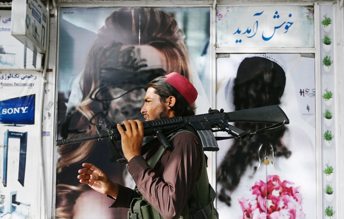 A Taliban fighter walks past a Kabul beauty salon, where images of women are defaced by spray paint.