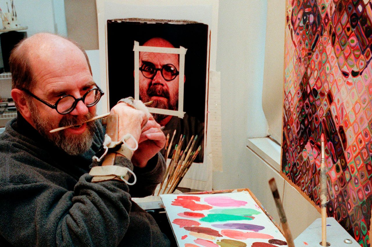 Chuck Close using a hand brace to hold his paint brush in 1996, following his spinal aneurysm.