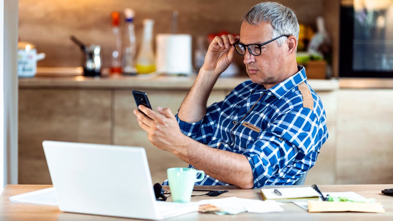 underscored man with glasses looking at cell phone and laptop