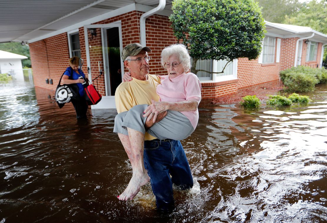 In the aftermath of Hurricane Florence in 2017, Bob Richling carries Iris Darden out of her flooded North Carolina home as her daughter-in-law, Pam Darden, gathers her belongings.