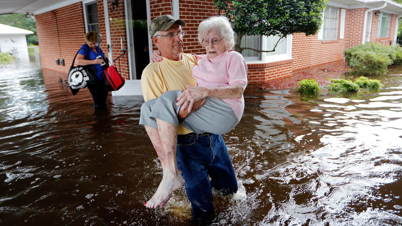 In the aftermath of Hurricane Florence in 2017, Bob Richling carries Iris Darden out of her flooded North Carolina home as her daughter-in-law, Pam Darden, gathers her belongings.
