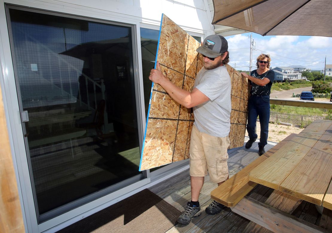 James Masog, center, and Gary Tavares move particle board into place to board up the sliding glass doors of a client's house in Charlestown, Rhode Island, on Saturday.