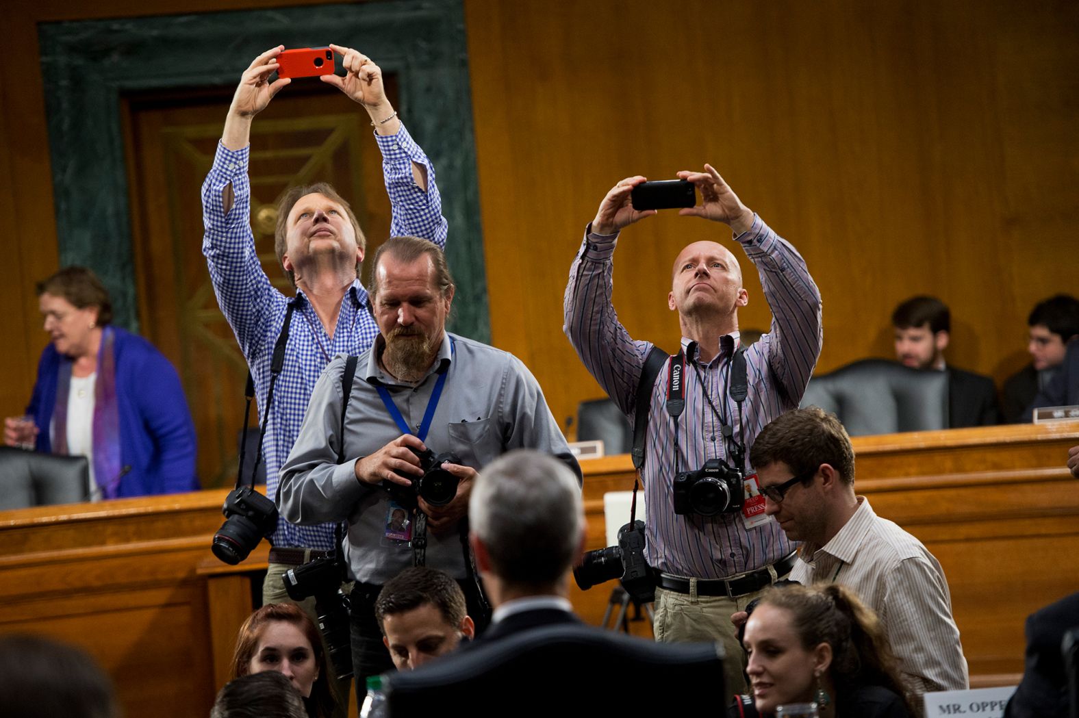 Photographers use iPhones to take photos of Cook during a break in a Senate hearing held by the Homeland Security and Governmental Affairs Subcommittee on Investigations in 2013. Cook and other Apple officials were on hand to explain the company's filings after the subcommittee accused Apple of tax avoidance.