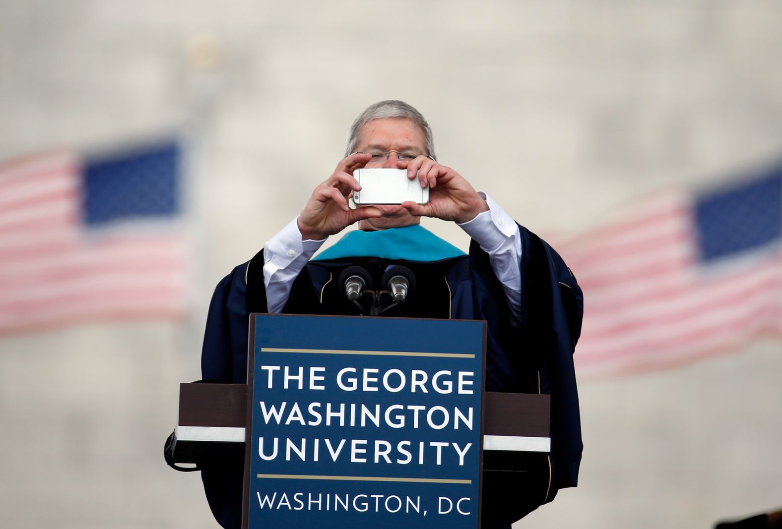 Cook takes a photo with his iPhone while addressing graduates during George Washington University's commencement exercises on the National Mall in May 2015. The university awarded Cook with an honorary doctorate of public service.