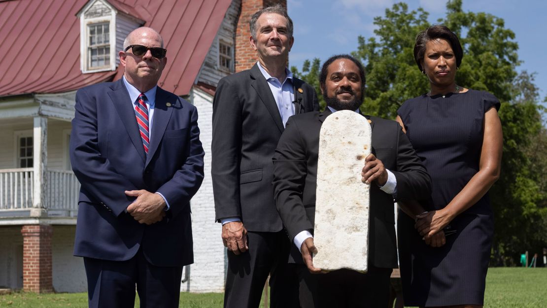 Nathan Burrell, with the Virginia Department of Conservation and Recreation, holds a grave marker and poses with, from left,  Govs. Larry Hogan  Ralph Northam and Washington, DC, Mayor Muriel Bowser after a ceremonial gravestone transfer Monday