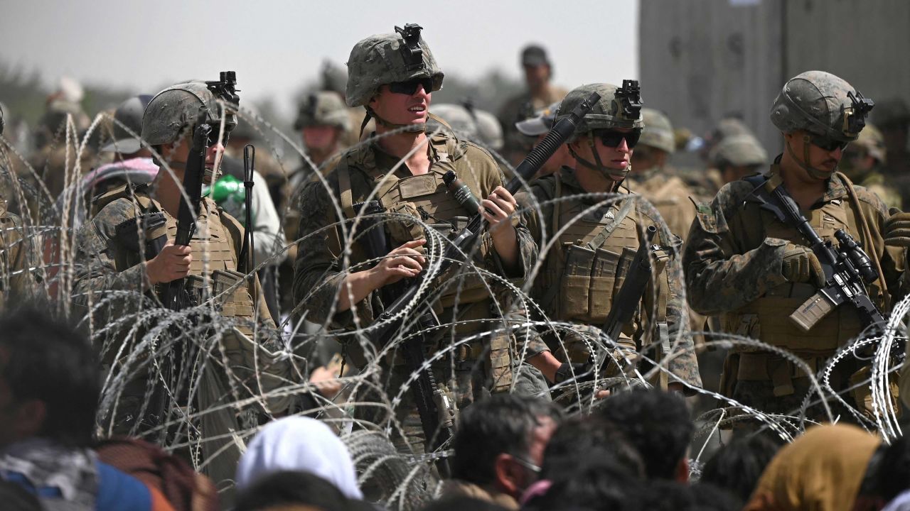 US soldiers stand guard behind barbed wire as Afghans sit on a roadside near the military part of the airport in Kabul on August 20, 2021