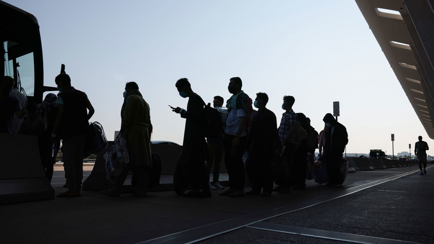 People who were evacuated from Kabul, Afghanistan, wait to board a bus at Washington Dulles International Airport in Virginia that will take them to a refugee processing center, on Wednesday, August 25, 2021.