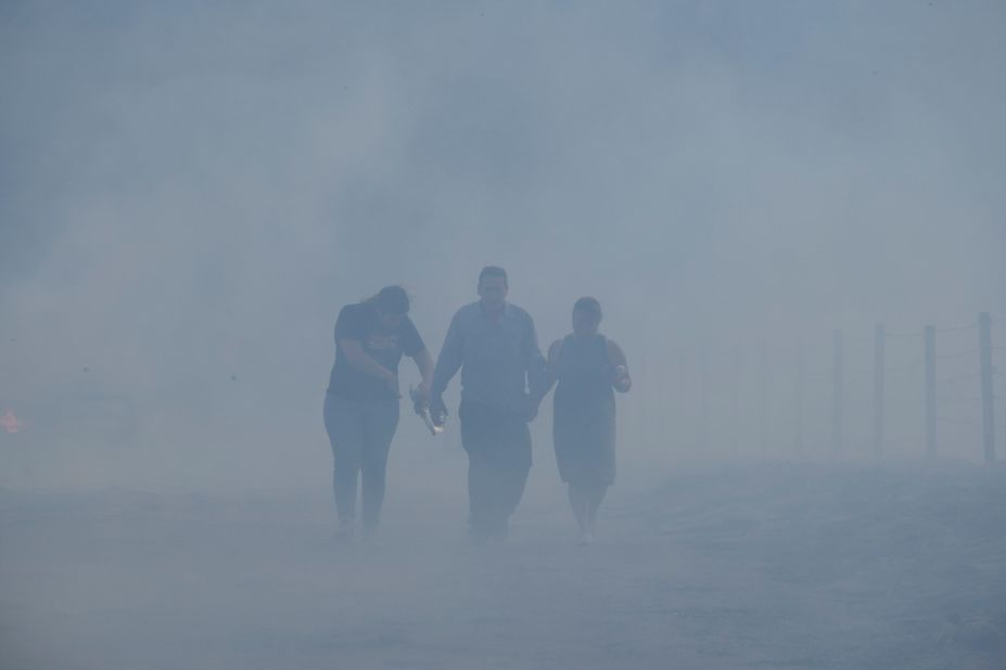 From left, Astrid Covarrubias, Jose Lamas and Maria Covarrubias walk through smoke after visiting their burned-out home in Lytle Creek on August 25.