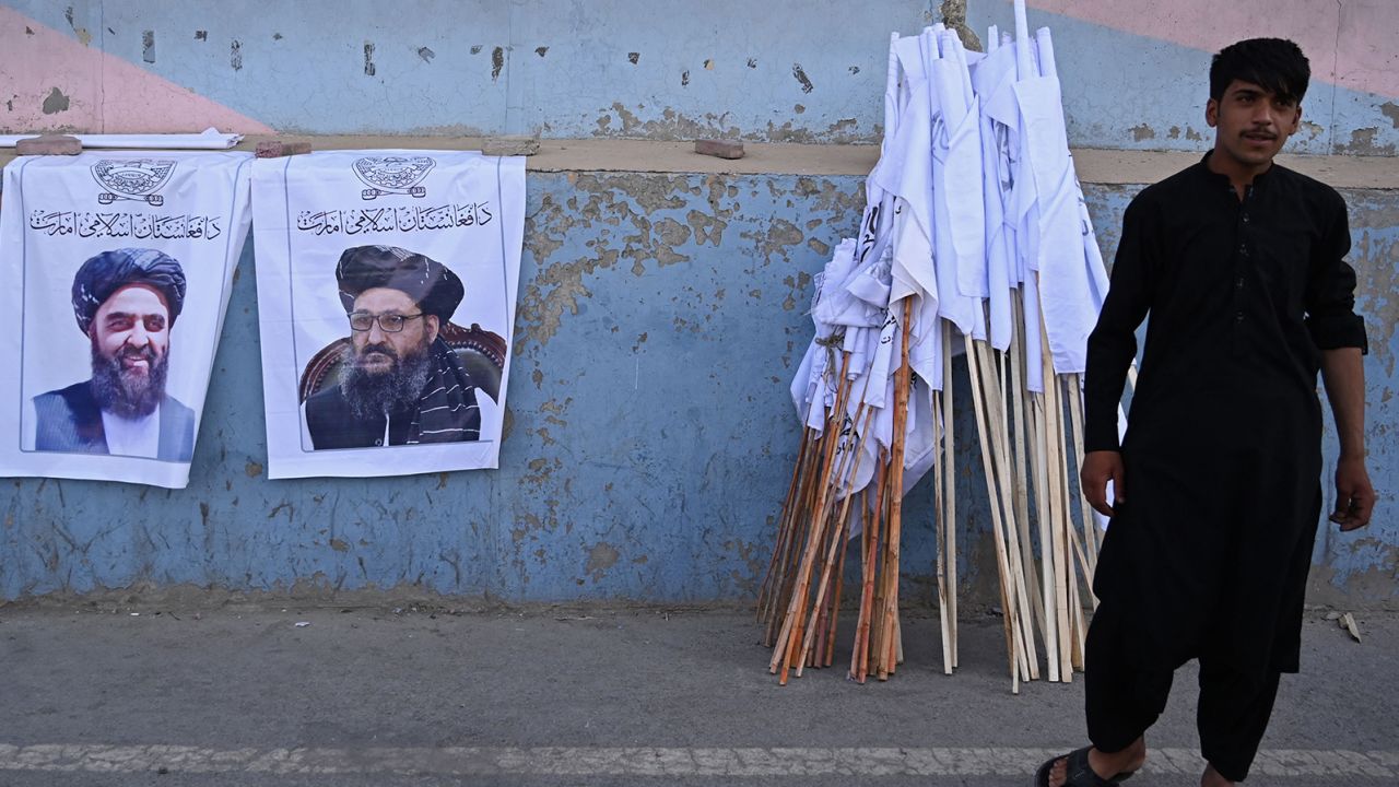 A vendor selling Taliban flags stand next to the posters of Taliban leaders Mullah Abdul Ghani Baradar and Amir Khan Muttaqi as he waits for customers along a street in Kabul on August 27.