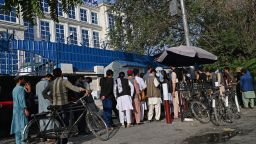 Afghan people stand in a queue as they wait for their turn to collect money from an ATM in front of a bank along a roadside in Kabul on August 21, 2021, days after the Taliban takeover of Afghanistan. 