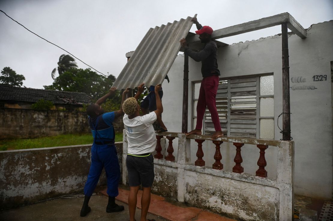 Men placed a corrugated metal sheet on the roof of a house under the rain in Batabano, Mayabeque province, about 60 km south of Havana, on August 27, 2021, as Hurricane Ida passed through eastern Cuba. 