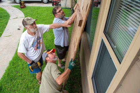 Larry Ackman, bottom, helps neighbor Mike Jackson, left, and his son Cody board up windows in Morgan City, Louisiana.