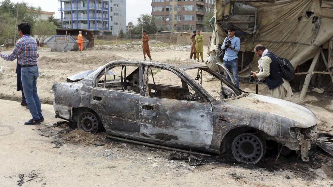 Journalists take photos of a destroyed vehicle where rockets were fired from in Kabul, Afghanistan, on August 30.