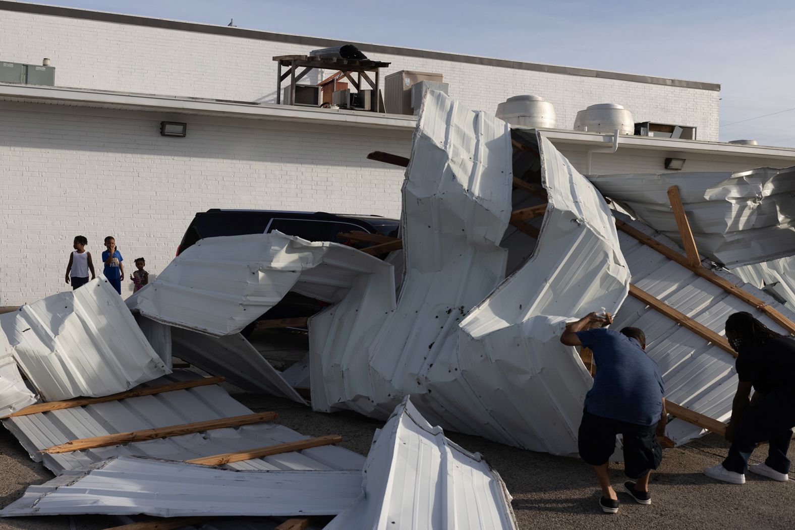 Siblings watch men assess damage outside a hotel in Houma on August 30.