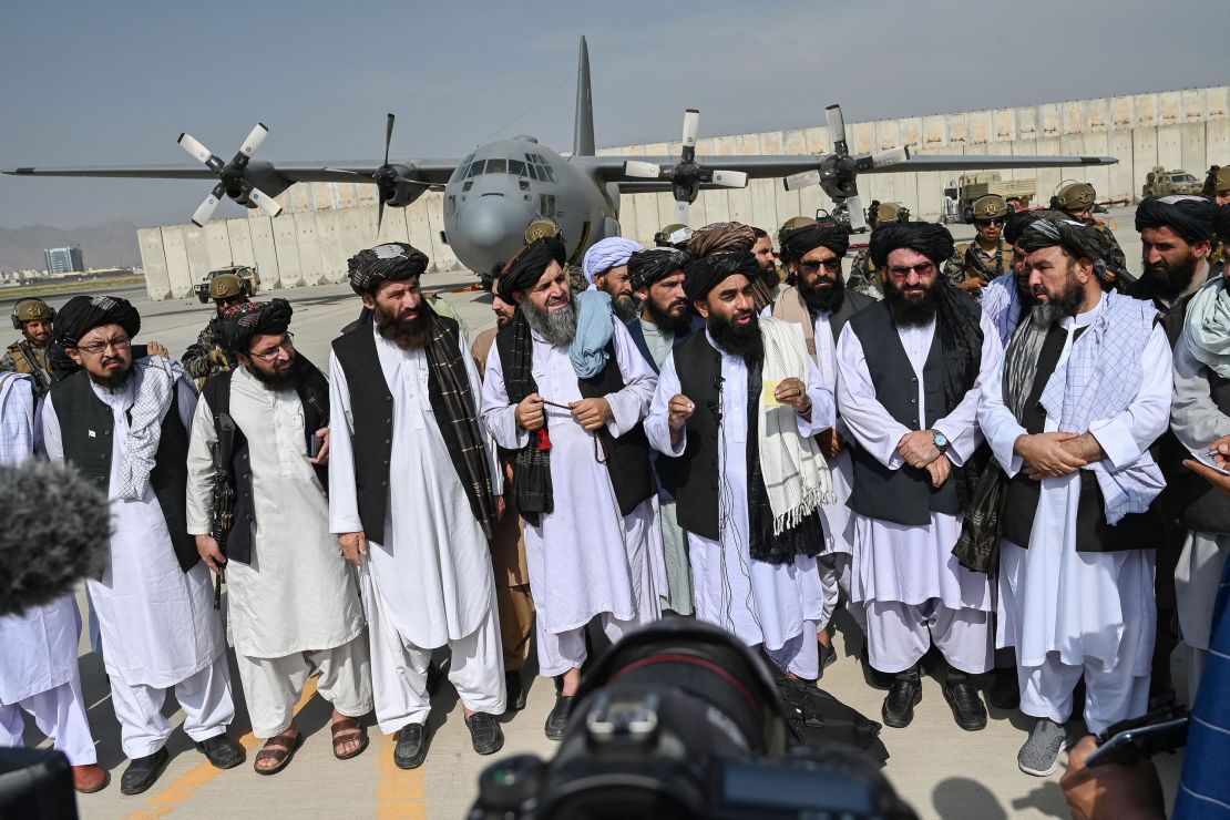 Taliban spokesman Zabihullah Mujahid (center, with shawl) speaks to the media at the airport. 