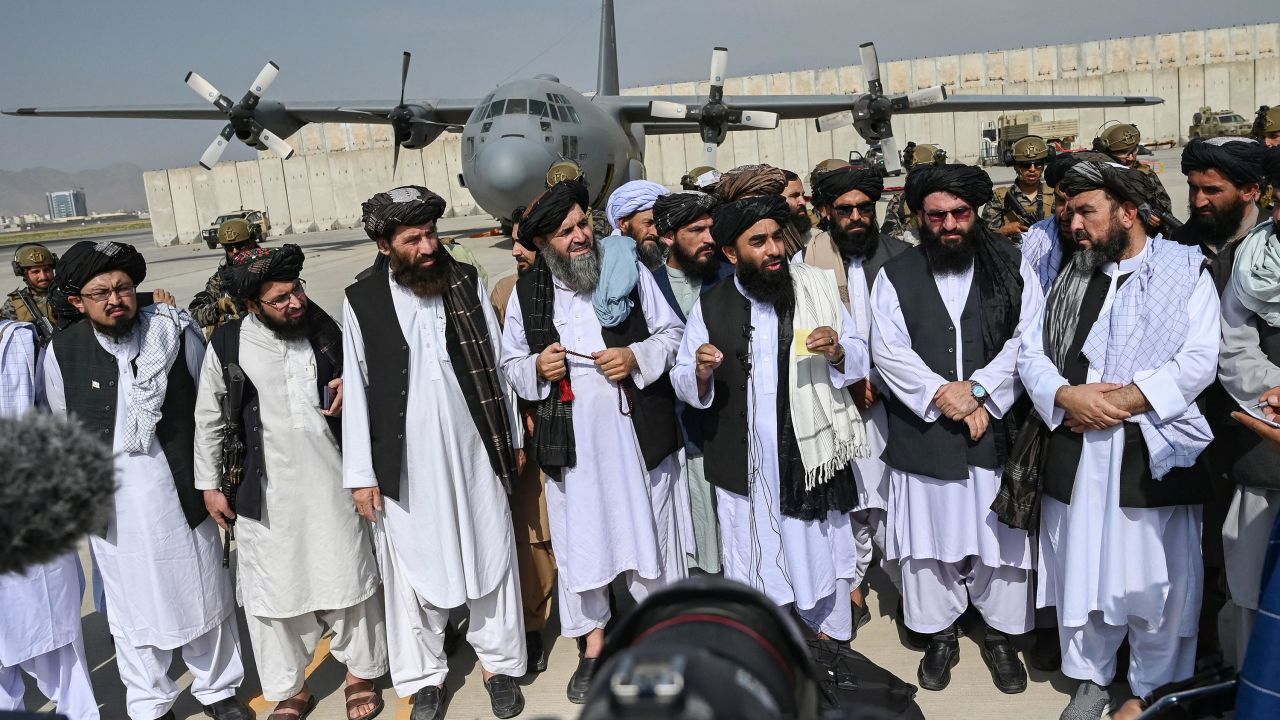Taliban spokesman Zabihullah Mujahid (center, with shawl) speaks to the media at the airport.