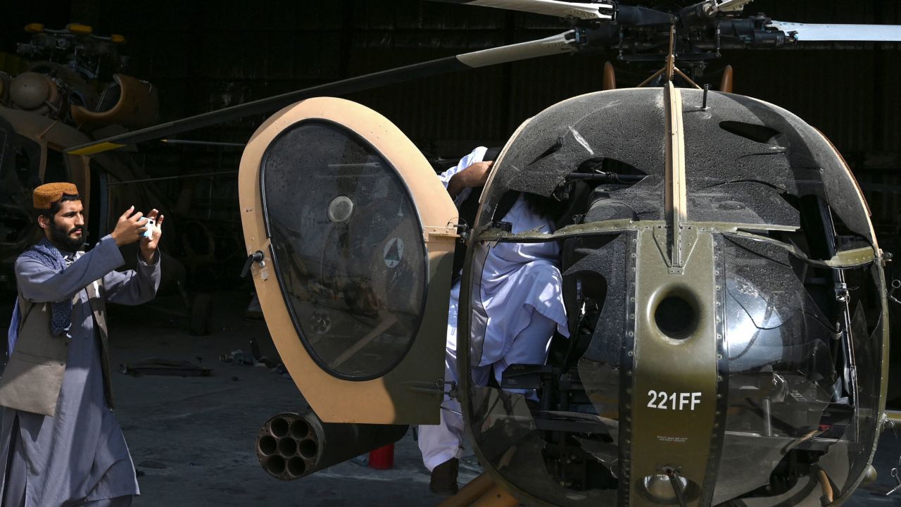 A Taliban fighter takes a picture of a damaged Afghan Air Force helicopter near a hangar at the airport.