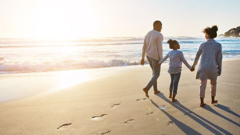 underscored family walking on beach sand next to ocean sunset