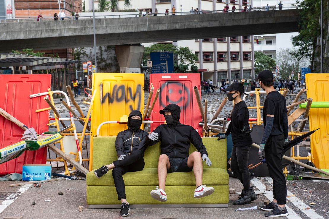 Anti-government protesters sit on a sofa while residents remove barricades built near HKU.