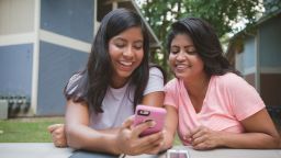 Hispanic mother and daughter texting on cell phone near apartments