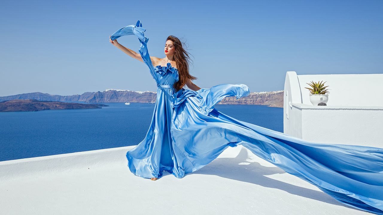 A woman in a blue "flying dress" poses in Santorini.