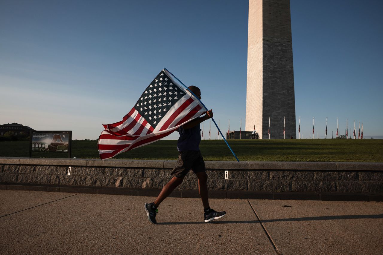 A jogger holds an American flag as he runs past the Washington Monument on Saturday.