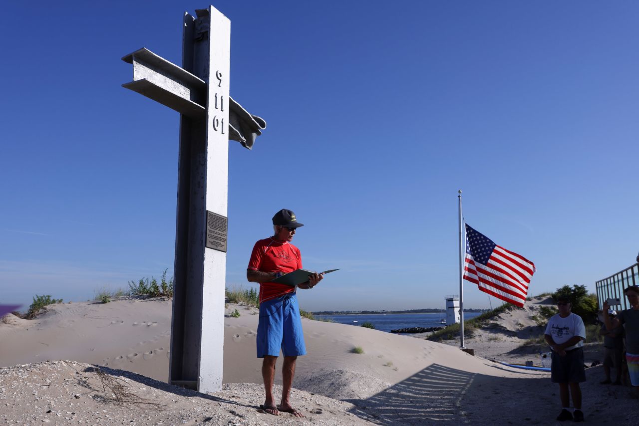 John Roberts leads community members in reading victims' names during a service at the 9/11 Breezy Point Memorial in New York at the time the first plane struck the North Tower of the World Trade Center. The cross is made of steel from the collapsed building.