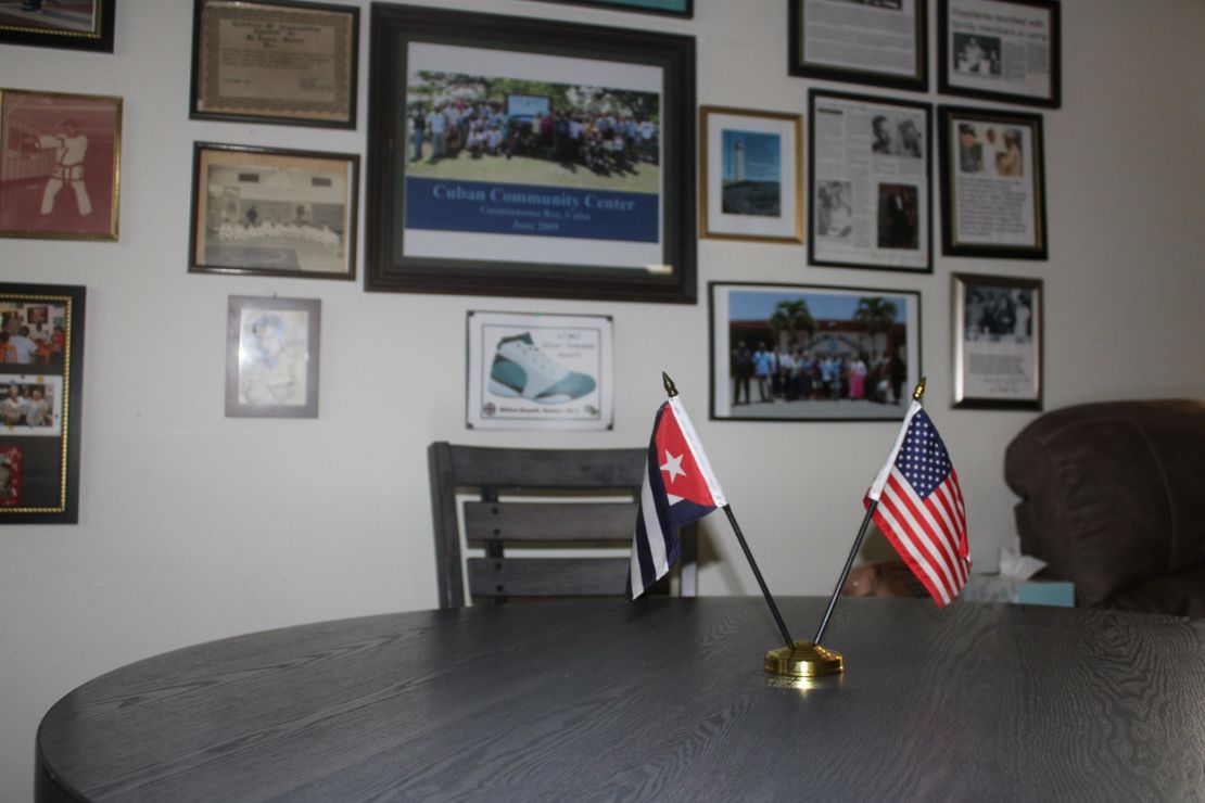 Inside the Cuban Community Center at US Naval Station Guantánamo Bay. The main room includes a wall of photos from the Cuban community. The small table in the room has both an American and Cuban flag displayed on it.