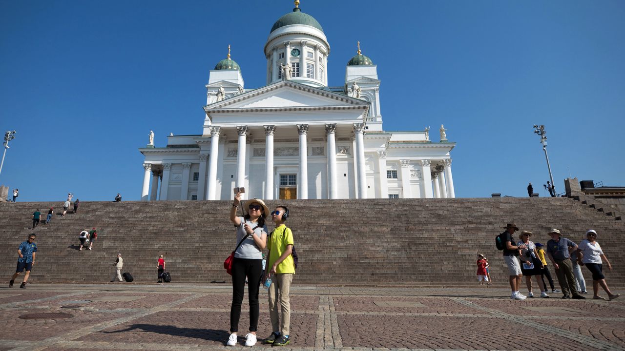 Tourists take a selfie photograph against the backdrop of the Helsinki Cathedral in Finland, which is using humor and rhymes to get its points across to visitors.