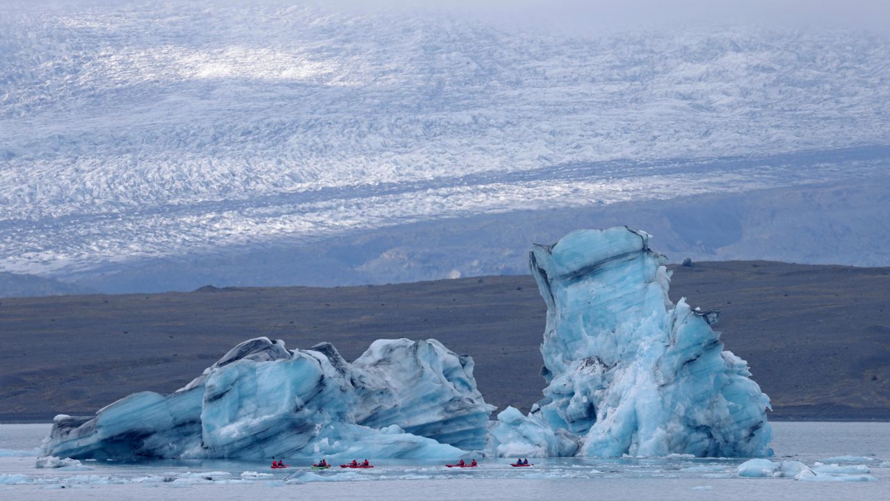 HOF, ICELAND - AUGUST 15: Tourists paddle kayaks past an iceberg that has broken off of receding Breiðamerkurjökull glacier, which looms behind, on Jokulsarlon lake on August 15, 2021 near Hof, Iceland. Breidamerkurjokull, among the biggest of the dozens of glaciers that descend from Vatnajokull ice cap, is melting, losing an average of 100 to 300 meters in length annually. Breidamerkurjokull's meltwater has created Jokulsarlon, which is now Iceland's biggest lake. Iceland is undergoing a strong impact from global warming. Since the 1990s, 90 percent of Iceland's glaciers have been retreating and projections for the future show a continued and strong reduction in size of its five ice caps.   (Photo by Sean Gallup/Getty Images)
