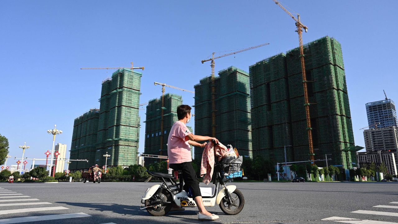 TOPSHOT - A woman rides a scooter past the construction site of an Evergrande housing complex in Zhumadian, central Chinas Henan province on September 14, 2021. (Photo by JADE GAO / AFP) (Photo by JADE GAO/AFP via Getty Images)